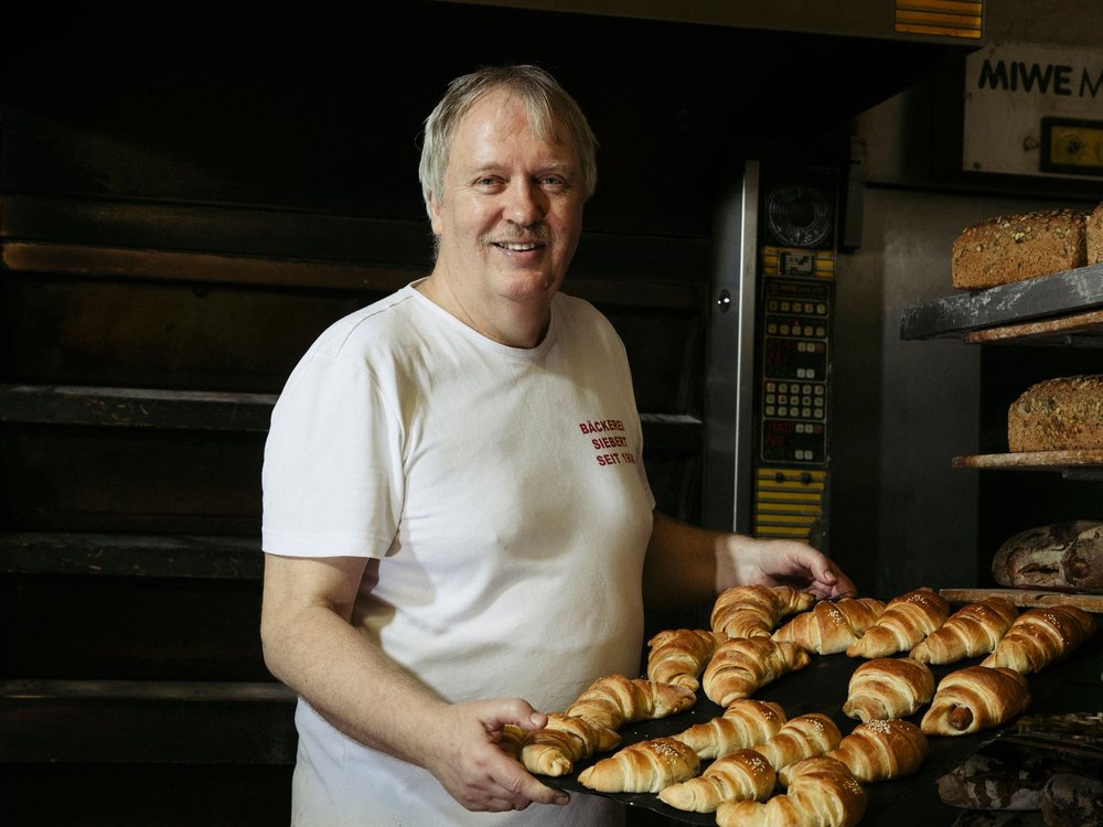 Bäcker präsentiert lächelnd ein Blech frisch gebackener Croissants