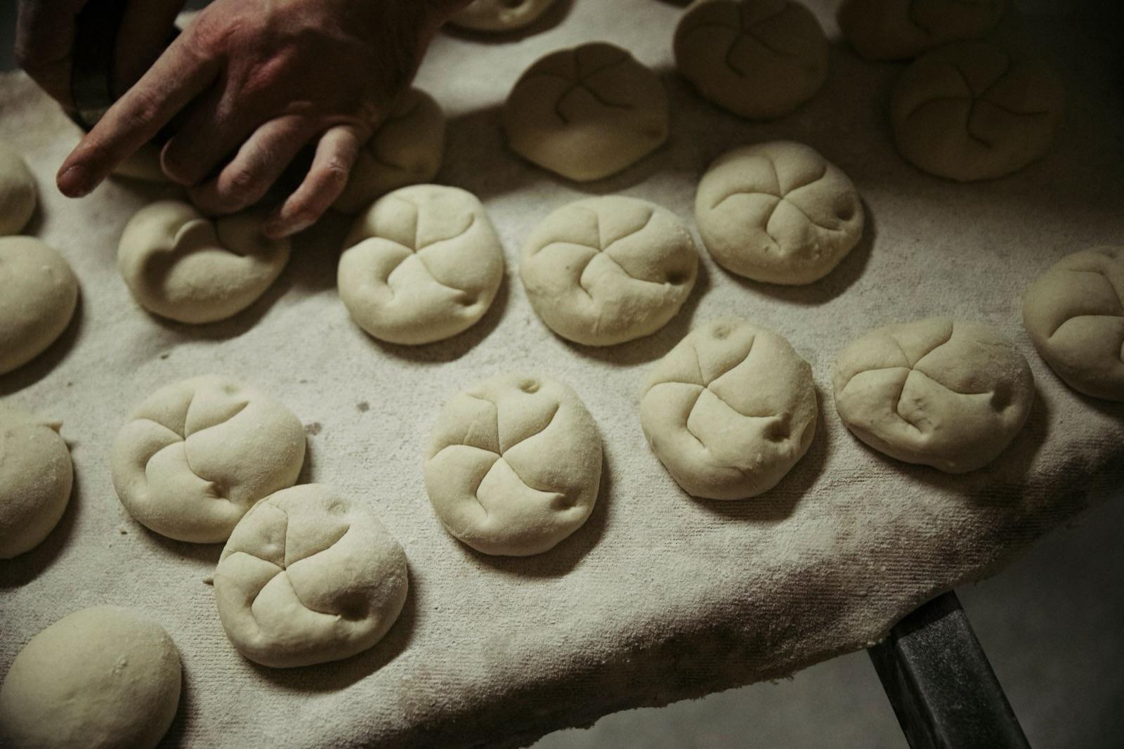 Bäckerin schlingt frische Brötchen von Hand auf dem Arbeitstisch